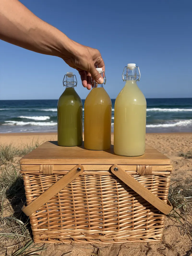 A hand placing bottled cocktails into a wicker picnic basket at the beach