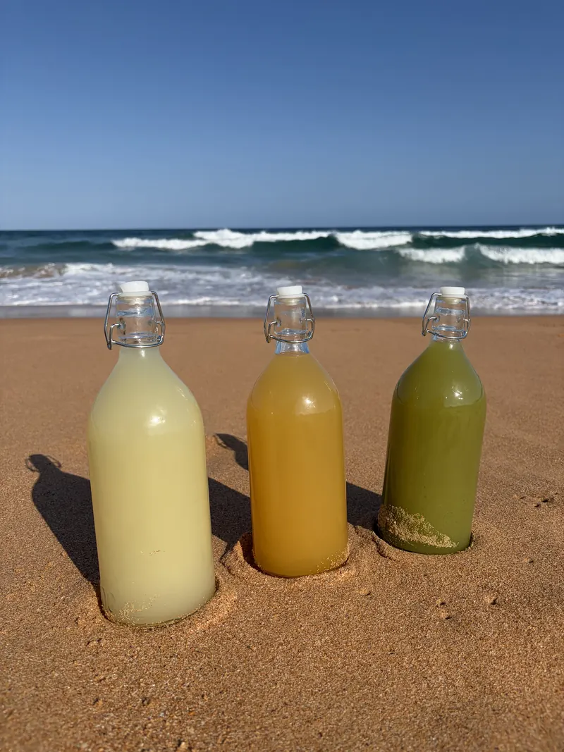 Three bottles of batched cocktails standing in the sand at the beach