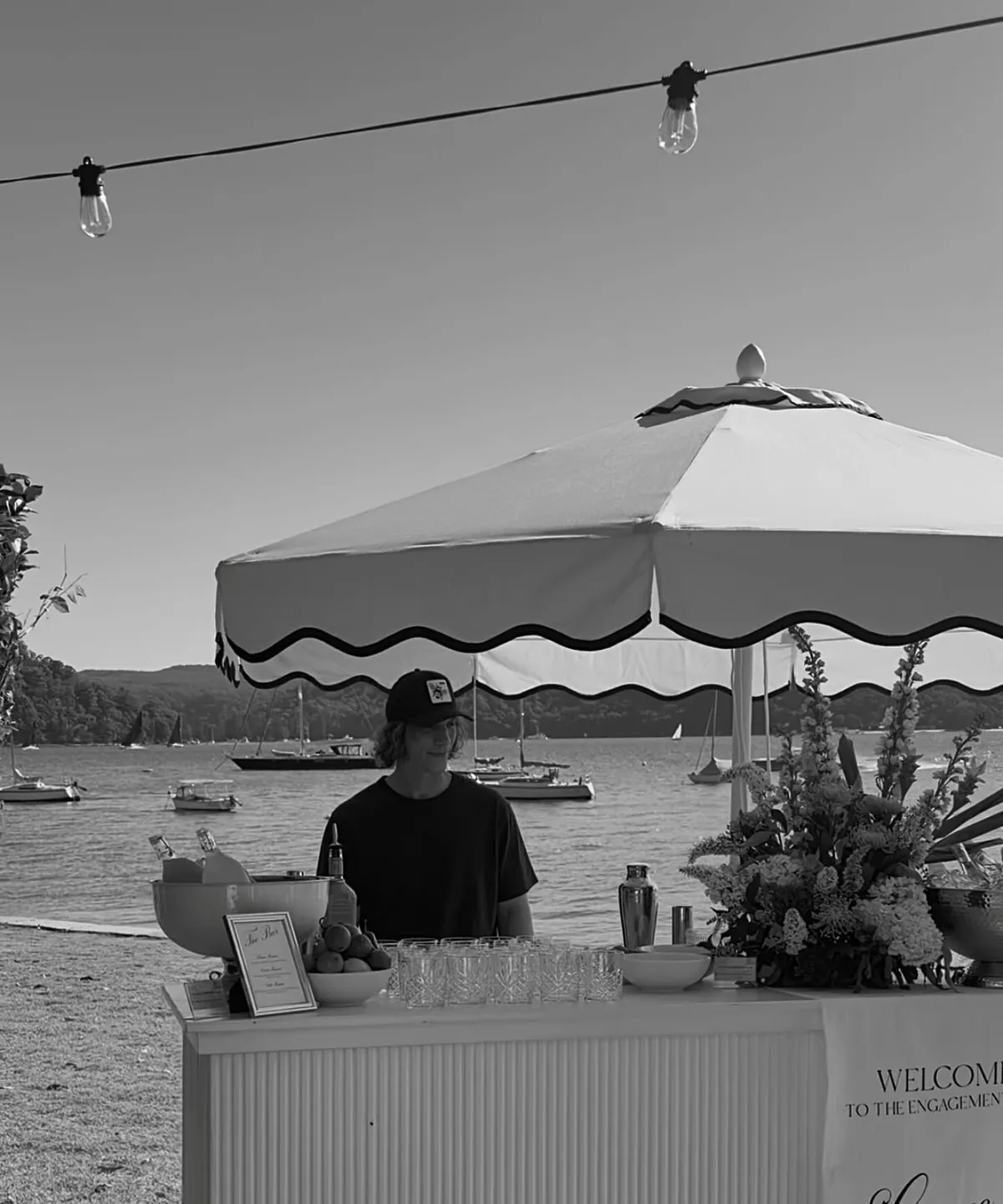 Ollie behind the scalloped-umbrella bar on Pittwater at golden hour, boats moored behind