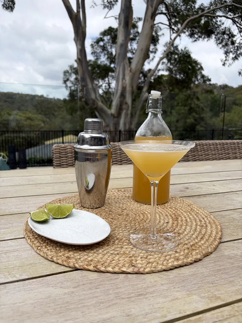 A margarita, shaker, lime wedges and a dish of salt on a jute mat
